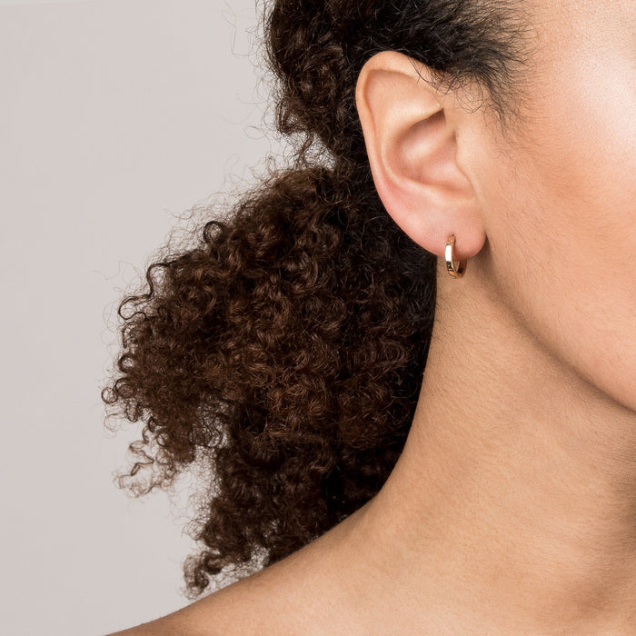 Model. Close up of woman wearing gold hoop earrings on white background