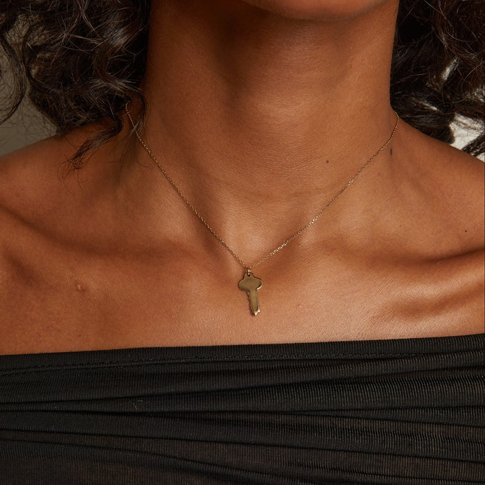 Model. Necklace with a key pendant worn by a person in a black top.