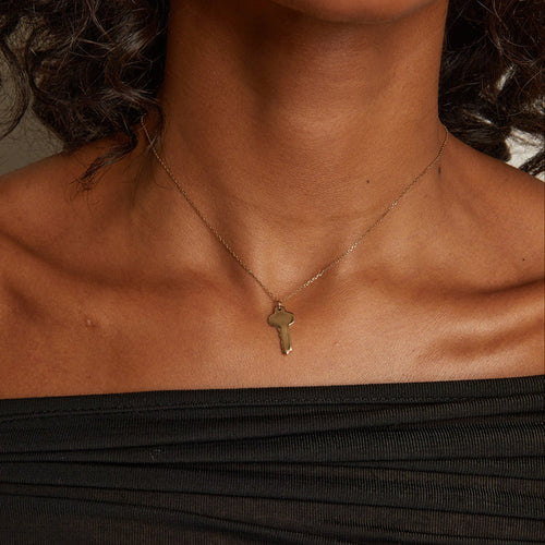 Model. Necklace with a key pendant worn by a person in a black top.