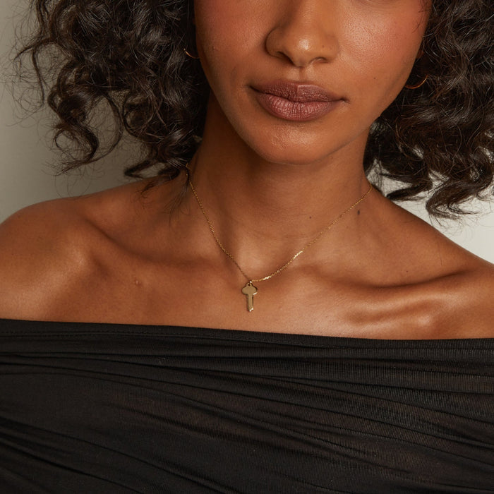 Model. Woman wearing a gold necklace with a pendant against a neutral background