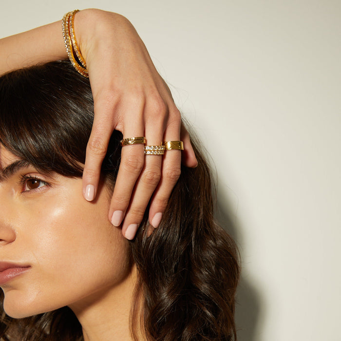 Model. Woman wearing gold jewelry including rings and a bracelet on a neutral background