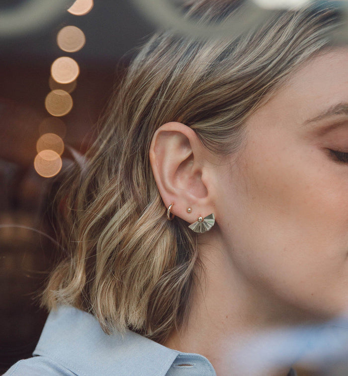Model. A close-up lifestyle shot of a woman wearing gold earrings on outdoors.
