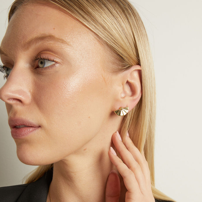 Model. A close-up lifestyle shot of a woman wearing gold fan stud earrings on white background.