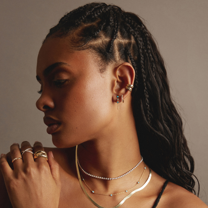 Model Woman with braided hair wearing multiple necklaces and rings against a neutral background