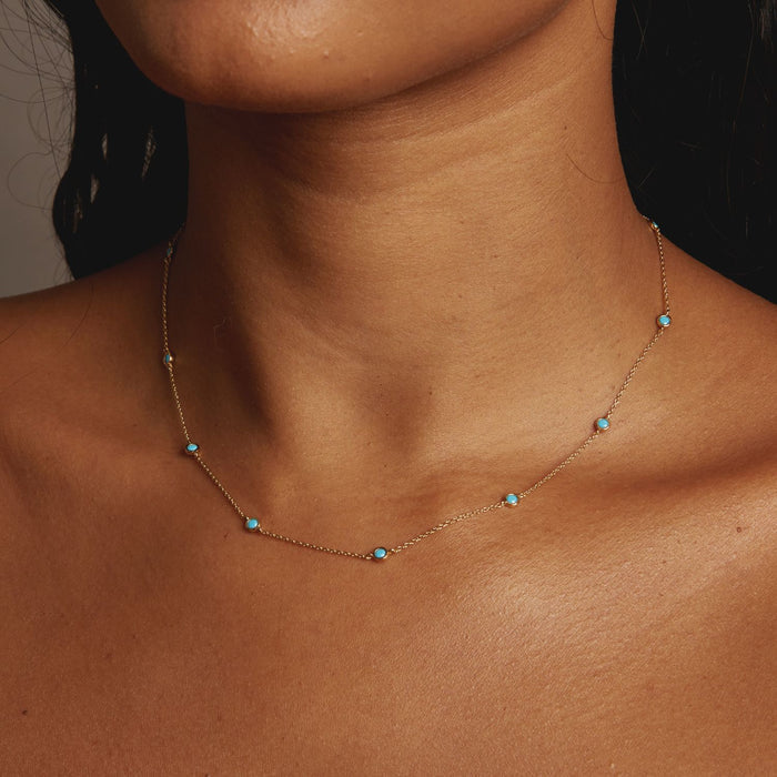 Model. Necklace with turquoise stones on a person's neck against a neutral background