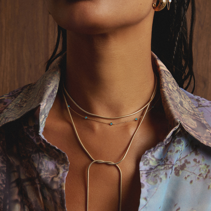 Model. Close-up of a person wearing a gold necklace with a floral-patterned shirt.