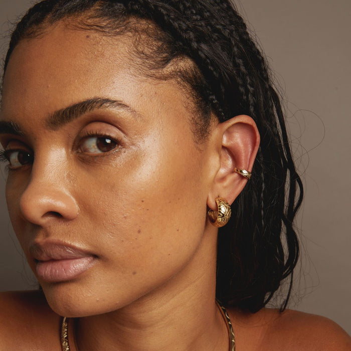 Model Close-up of a woman's face with gold earrings and necklace against a neutral background
