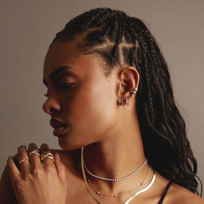 Model Woman with braided hair wearing multiple necklaces and rings against a neutral background