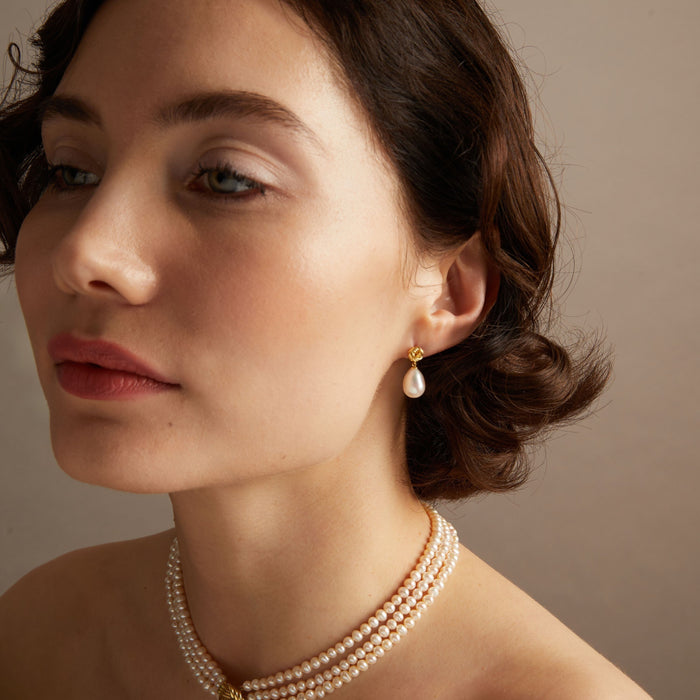 Pearl knot earrings and necklace on woman with neutral background.