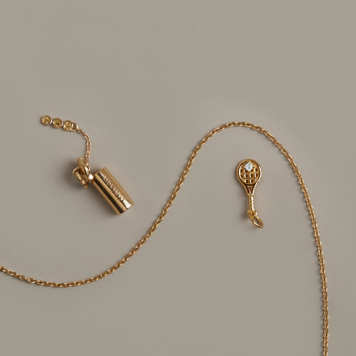 Model. Gold necklace with a tennis racket charm on a beige background