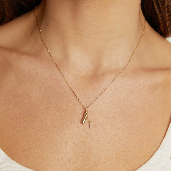Model. Gold necklace with a pendant on a person wearing a white top