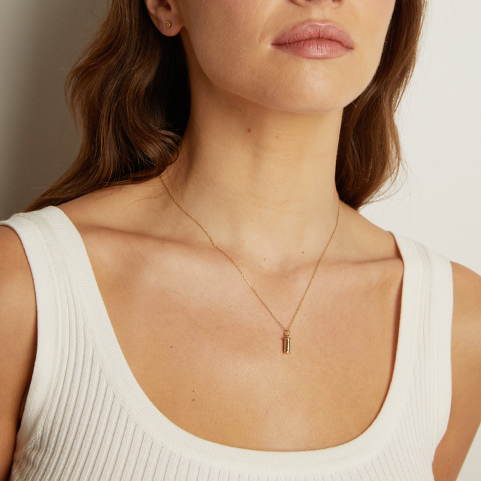 Model. Close-up of a woman wearing a gold necklace with a pendant.