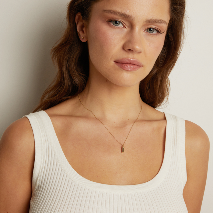 Model. Woman wearing a white tank top and gold necklace against a neutral background