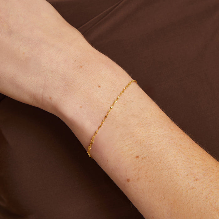 Model. Gold bracelet on a person's wrist against a brown background