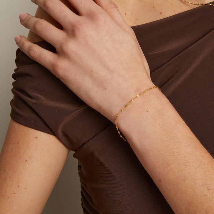 Model. Person wearing a brown dress with a gold bracelet and necklace against a neutral background