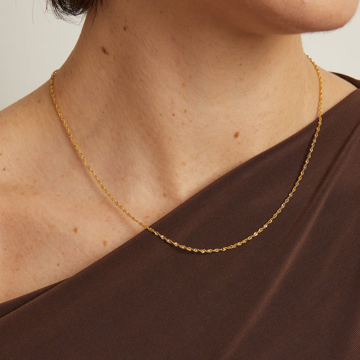 Model. A person wearing a brown shirt with a gold fine chain necklace.
