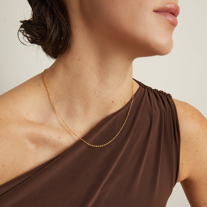 Model. Close-up of a person wearing a gold necklace with a neutral background