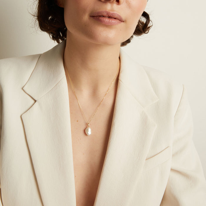 Model Person wearing a pearl necklace with a cream blazer against a neutral background