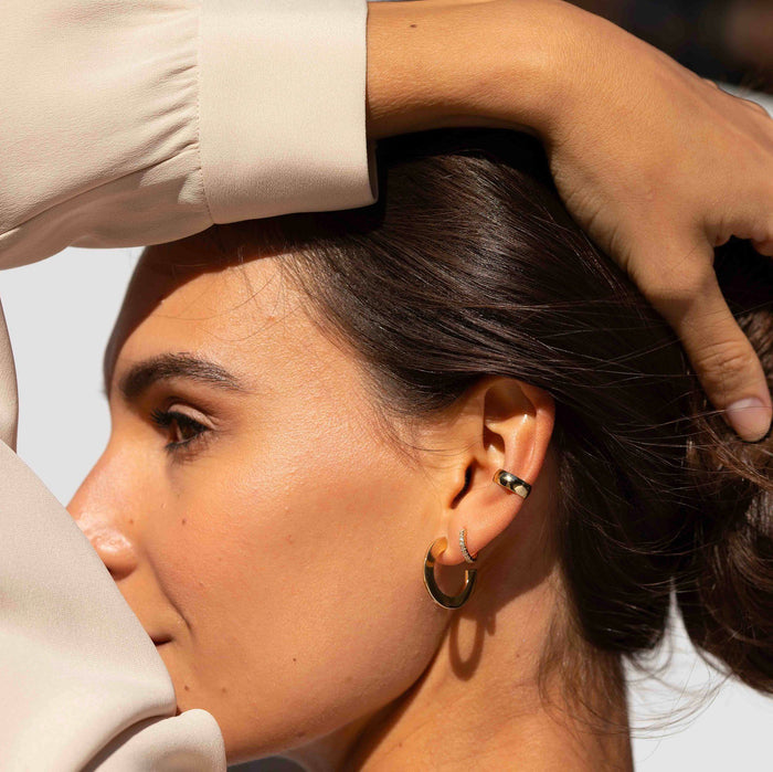 Bold Ear Cuff On Model Lifestyle. A close-up side profile shot of a woman wearing a two hoop earrings earrings and a gold ear cuff