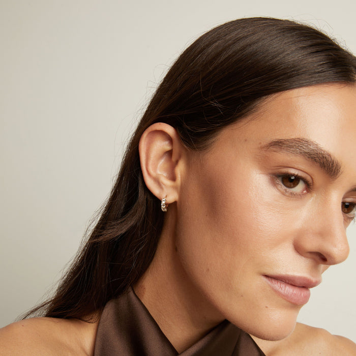 Model. Close up of woman wearing a white sapphire huggie earring on a neutral background.