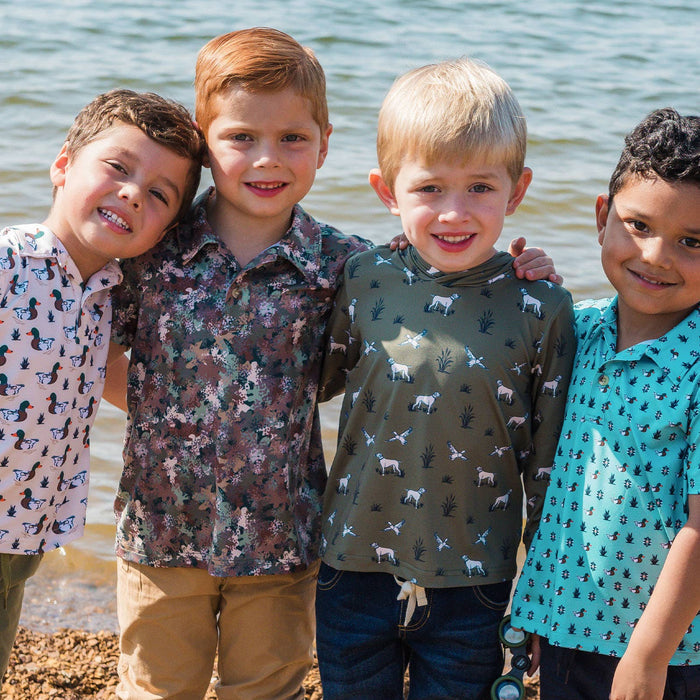 Four children standing together on a beach, wearing patterned shirts and boots.