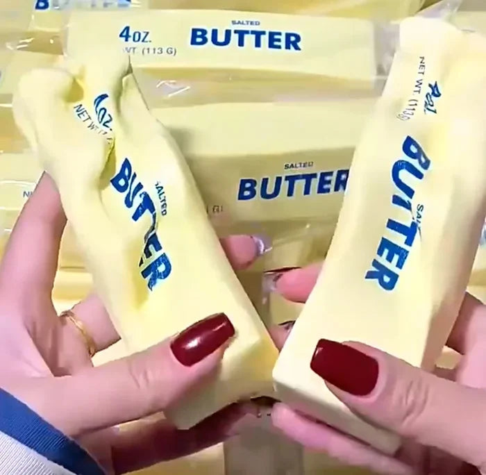 Two hands holding sticks of butter in front of packaged butter sticks. The butter sticks are pale yellow with blue text reading 'BUTTER' and 'SALTED'.