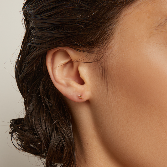 Model. Close-up of an ear with a gold earring against a neutral background