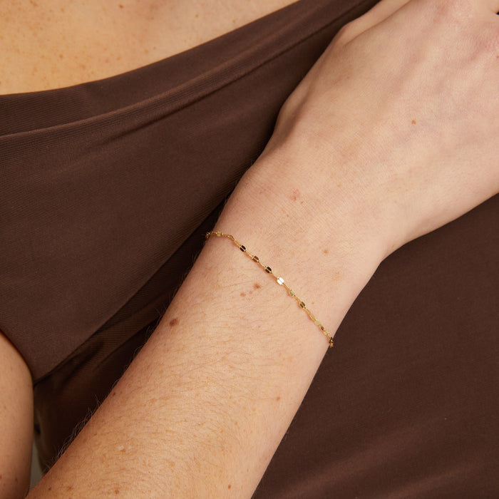 Model. Gold bracelet on a wrist with a brown fabric background
