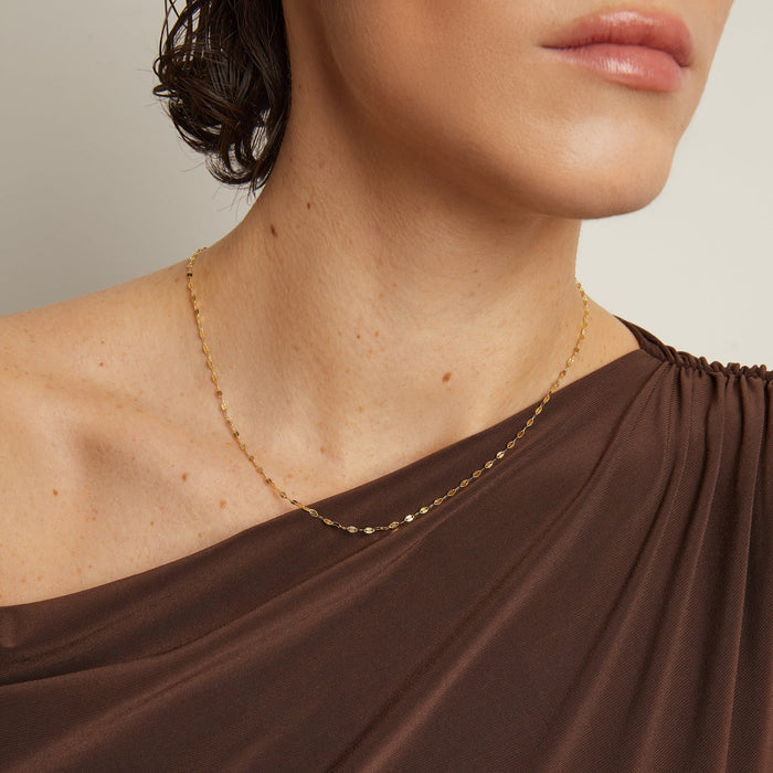 Model. Close-up of a person wearing a gold necklace with a plain background