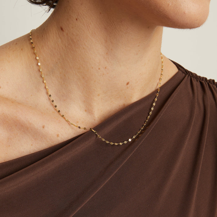 Model. Close-up of a person wearing a gold necklace with a neutral background
