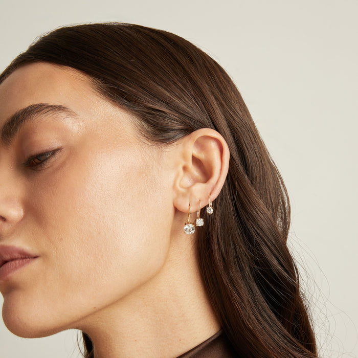 Model. Close up of a woman wearing 3 gold hoop earrings with white gemstones on neutral background.