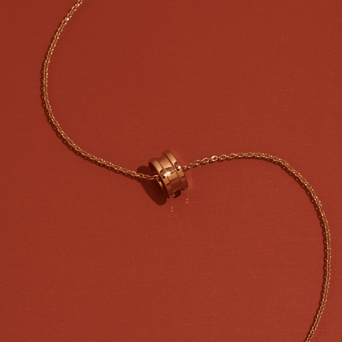 Flatlay Model Close-up of a gold column pendant necklace resting on a warm orange surface