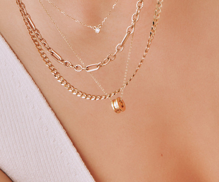 Lifestyle Model Close-up of a woman wearing a white top and layered gold necklaces, prominently featuring a gold column ring pendant