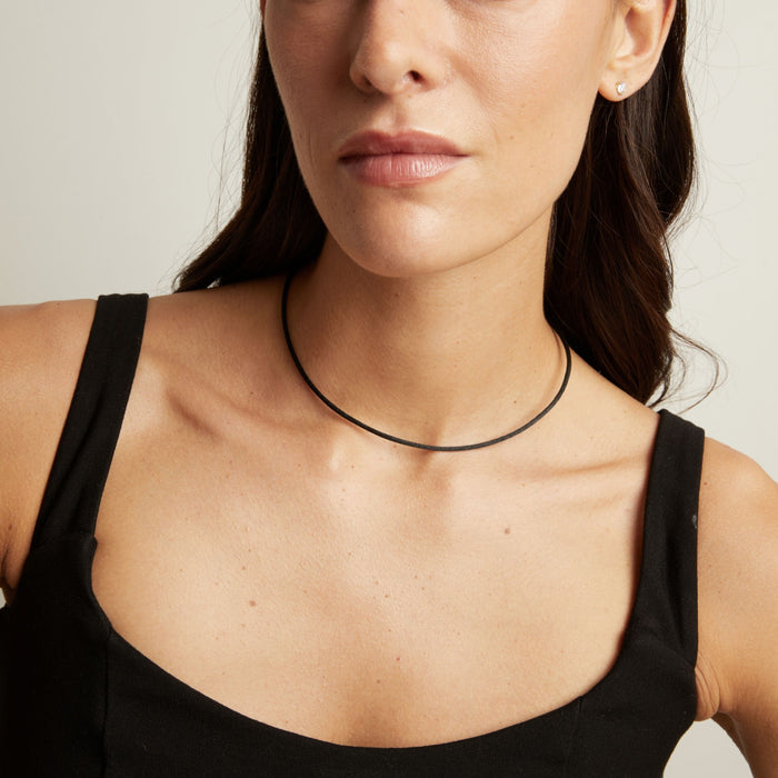 Model. A close-up of a model wearing a thin black cord necklace, paired with a black camisole top against a light neutral background.