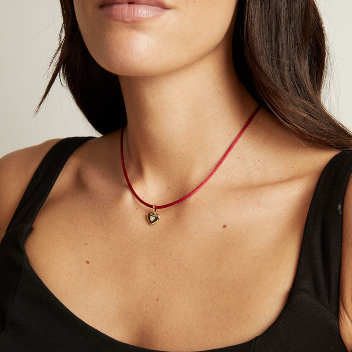 Model. A close-up of a model wearing a thin cord necklace with a heart pendant, showing the necklace against her neck and upper chest.