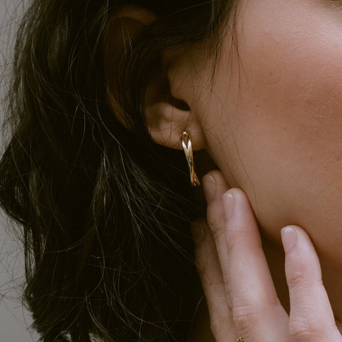 Lifestyle Model Close-up of a woman's profile showcasing a gold crossover hoop earring, with her hand delicately resting against her neck