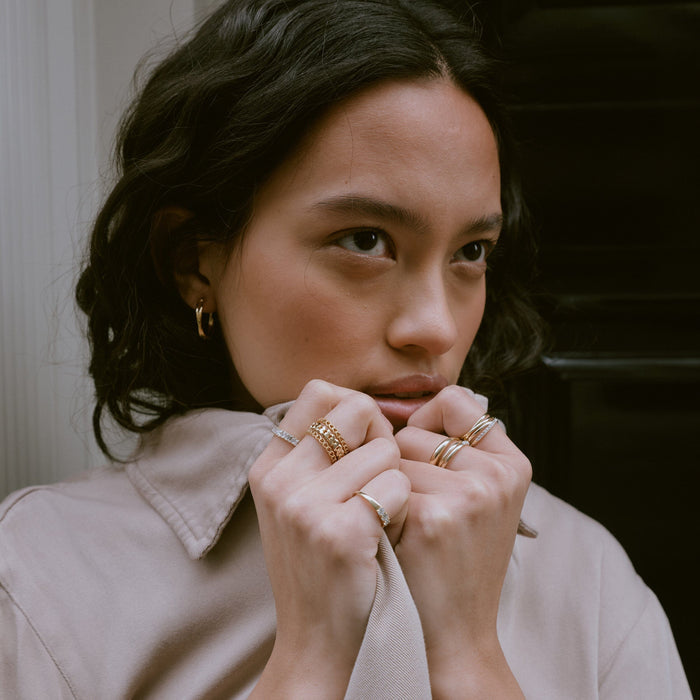 Lifestyle Model Close-up of a woman with her hands resting near her face, showcasing stacked gold and diamond rings alongside a small gold crossover hoop earring.