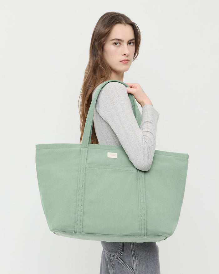 Dina Sage Travel Tote in sage green nylon, Lolo Pointelle Long-Sleeve Top in grey cotton, and Molly Workwear Jean in grey denim.