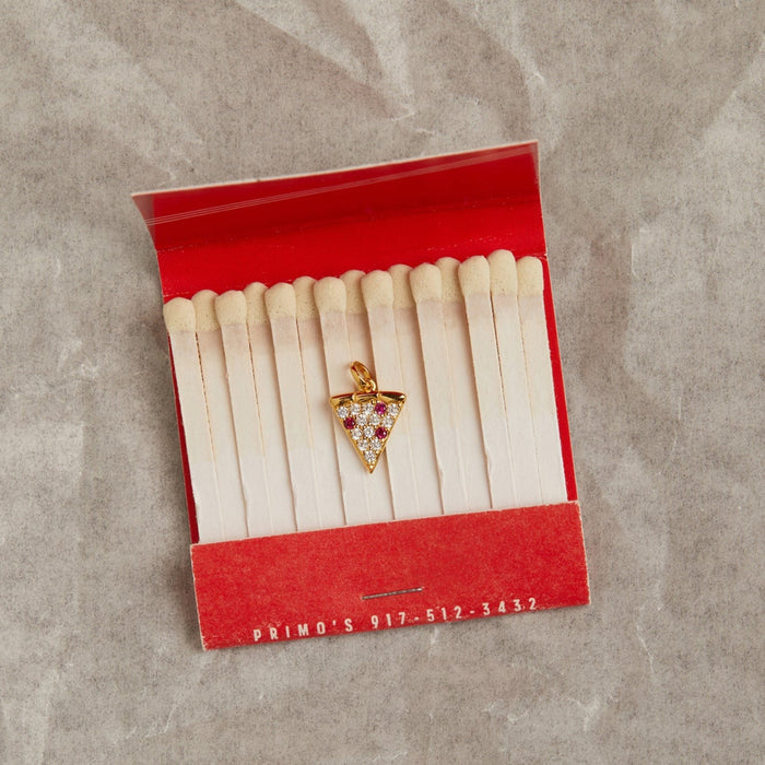 Model. Gold triangle-shaped pendant with red stones inside an open matchbox on a gray surface