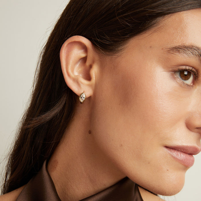 Model. Close up of woman wearing a gold bezel huggie earring on neutral background.