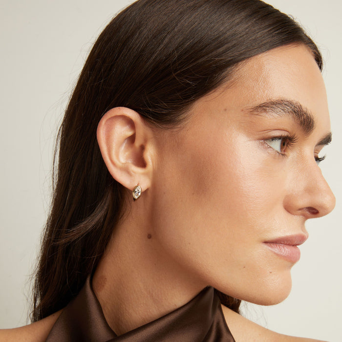 Model. Close up of woman wearing a gold bezel huggie earring on neutral background.