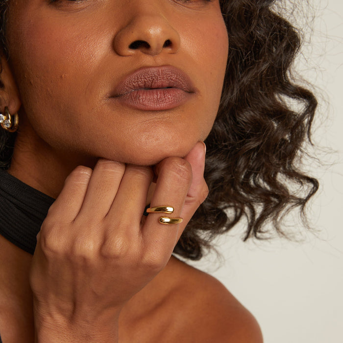 Model. Close-up of a woman's face with hand on chin, wearing gold rings and earrings.