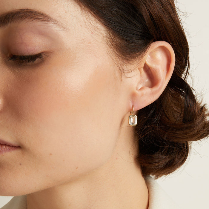 Model. Close-up of a woman wearing gemstone hoop earrings with a neutral background