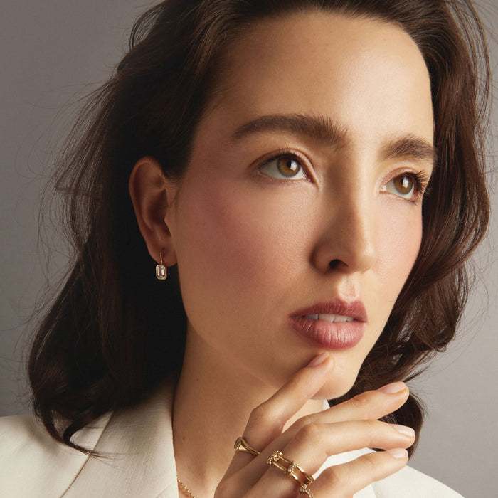 Model. Woman wearing drop earrings and stacked godl rings.