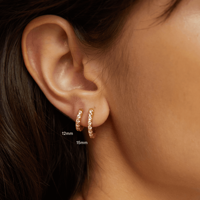 Model. Close up of two gold hoop earrings on ear.
