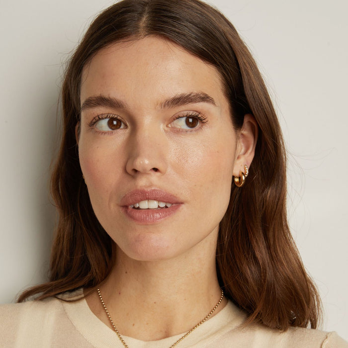 Model. Close-up of a woman with brown hair and gold earrings against a plain background