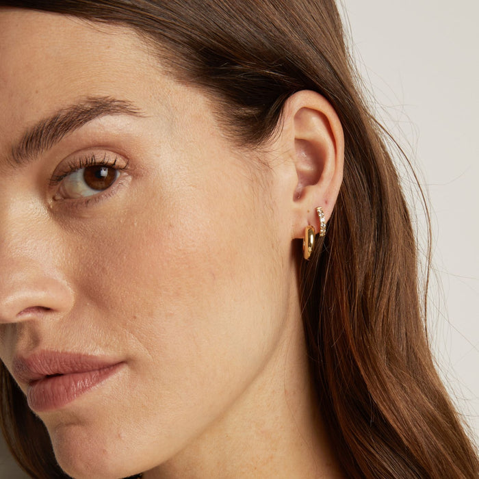 Model. Close-up of a woman wearing a gold earring with a heart design.