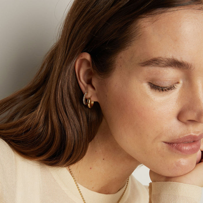 Model. Close-up of a woman wearing gold earrings and a necklace against a neutral background