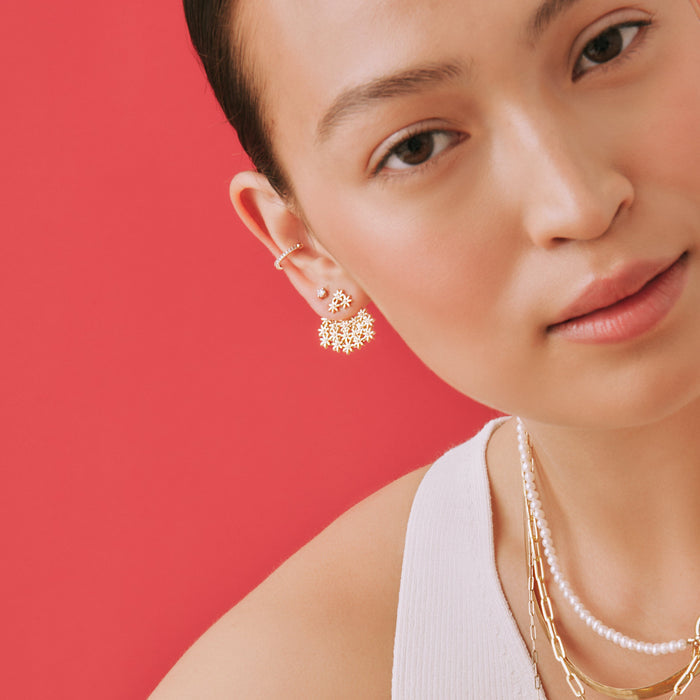 Lifestyle Model. A close-up lifestyle shot of a woman wearing statement gold stud earrings and cuff on a pink background.