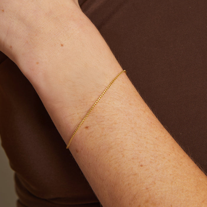 Model. Gold bracelet on a person's wrist against a brown background